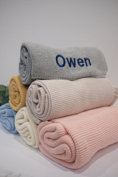 Personalised knit baby blanket colour options – grey, mustard, cream, blue and pink – custom embroidered name Owen shown on baby gift box blanket Australia